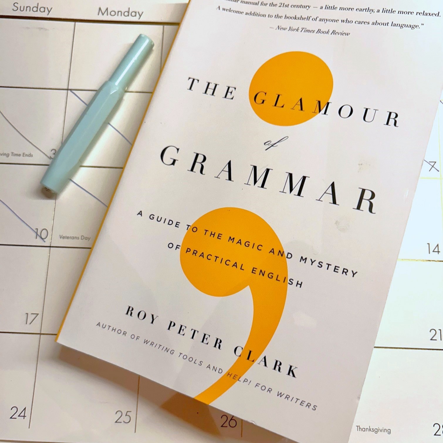 cover of the book THe Glamour of Grammar sitting ontop of a large paper calendar with a blue pen beside it.