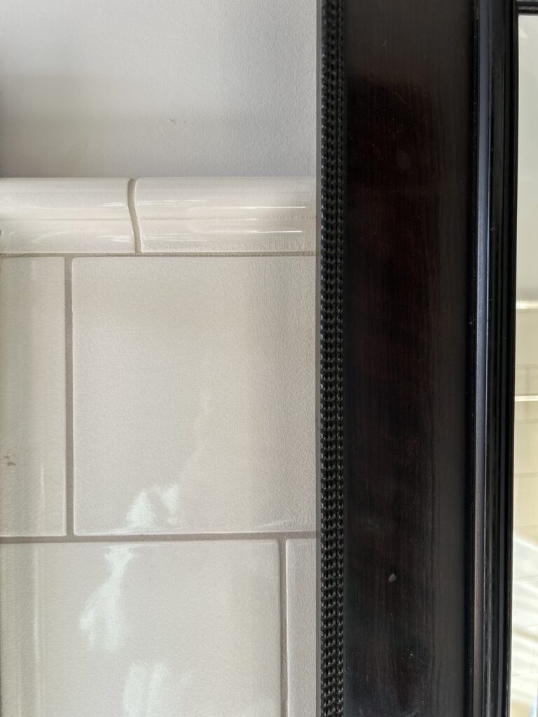 wall with subway tiles featuring a cap or rail at the top with edge of mirror at right