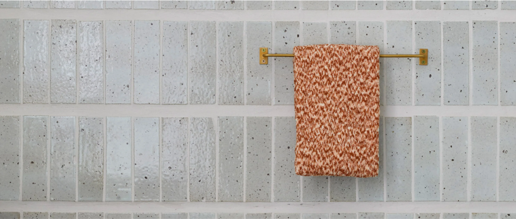 blue grey cle tiles installed in modern horizontal pattern with orange towel on brass rod on top