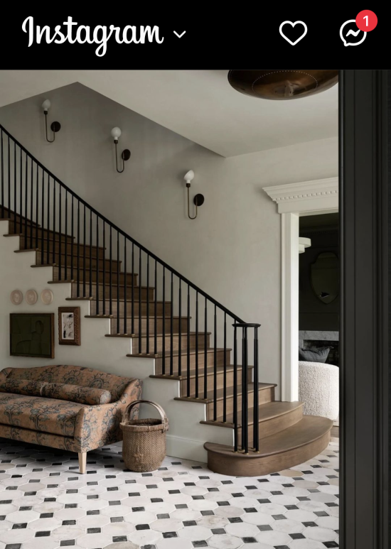 Foyer with transitional aesthetic has stone tiled floor, wood staircase and metal railing. Printed fabric sofa and an art collage create an eclectic interior.