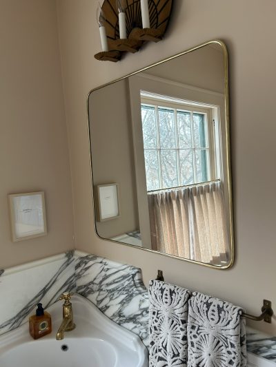 a powder room mirror and sconce above a white sink with marble splash