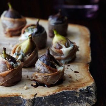 prosciutto wrapped figs on a rustic wood platter